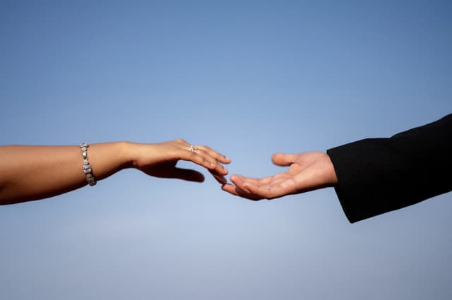 Hands reaching toward each other against a clear blue sky