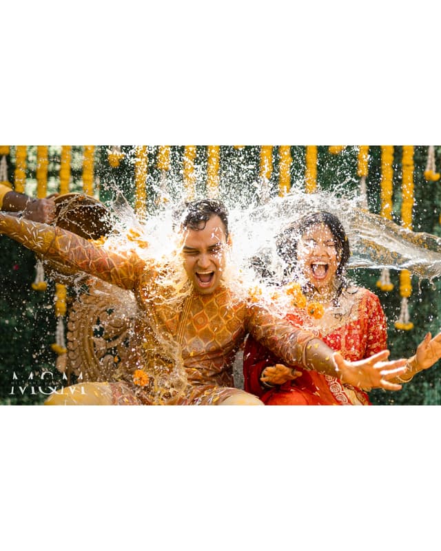 Couple laughing as water splashes during a Haldi celebration