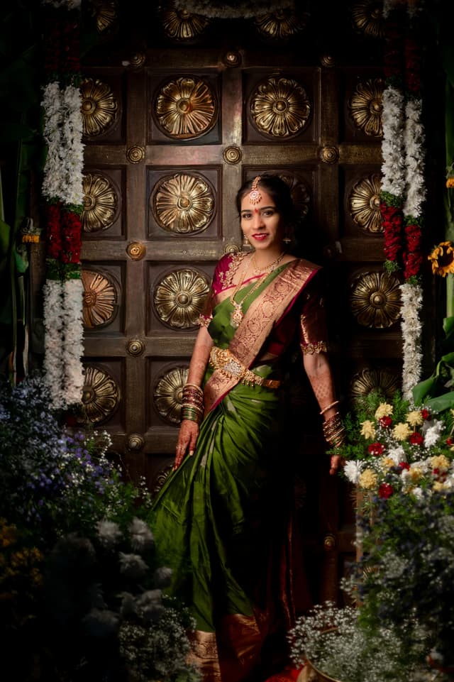 Bride standing in a green sari before a richly decorated backdrop