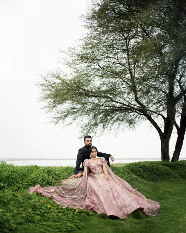 Couple seated beneath a tree with the bride's outfit spread around them