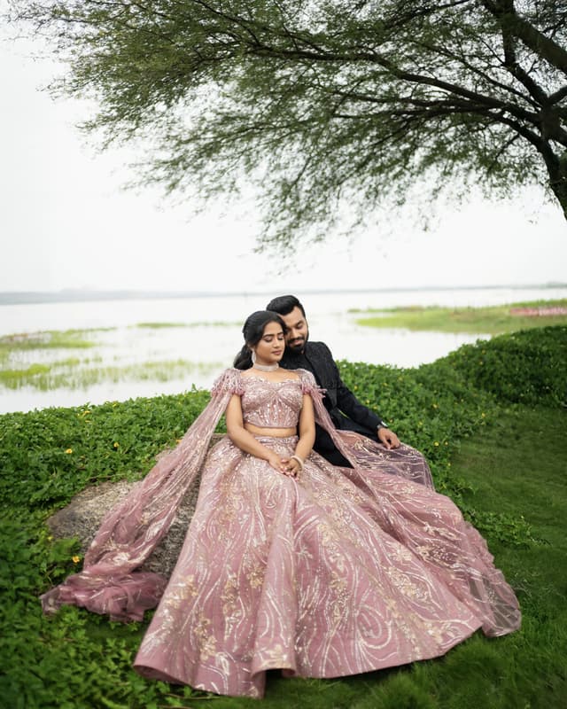 Couple seated together beneath a tree beside a quiet waterfront