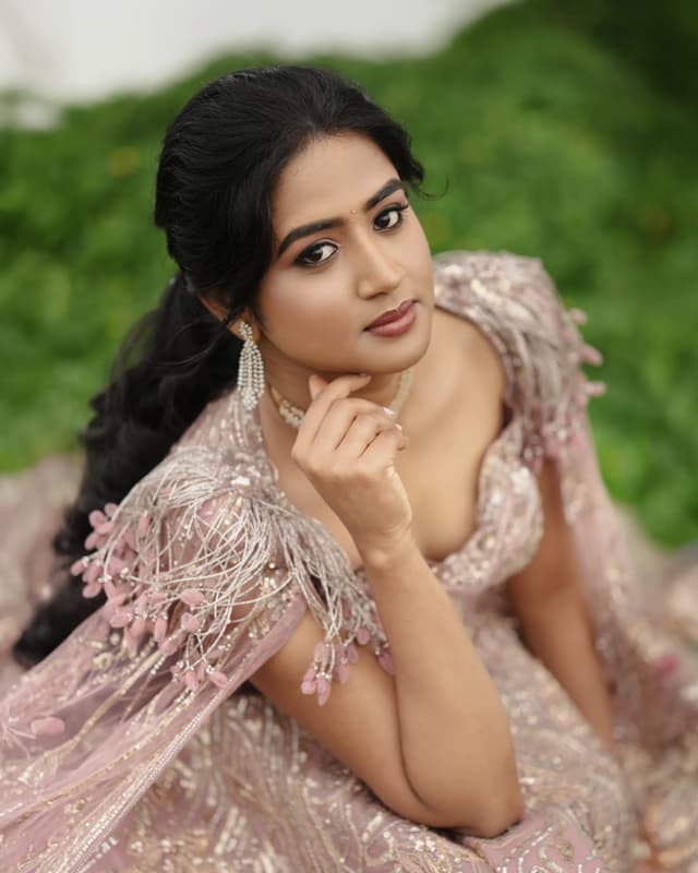 Bride in pink Sangeeth attire resting her chin on her hands outdoors