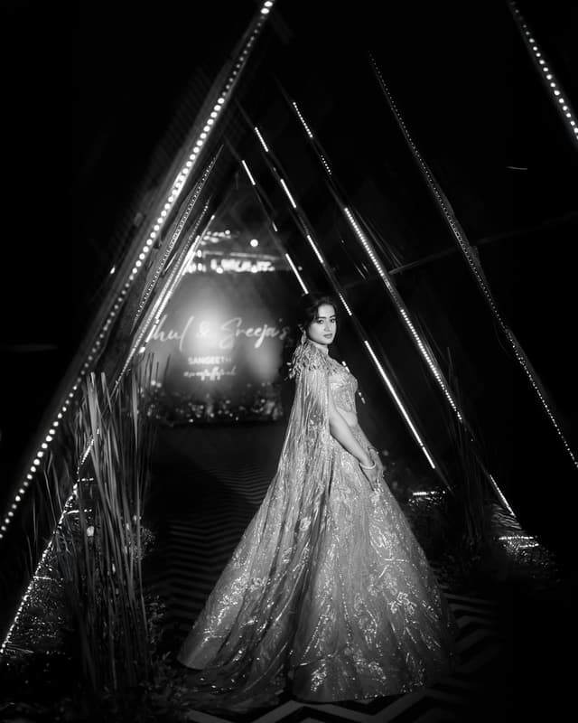 Black and white portrait of a bride standing beneath dramatic lights