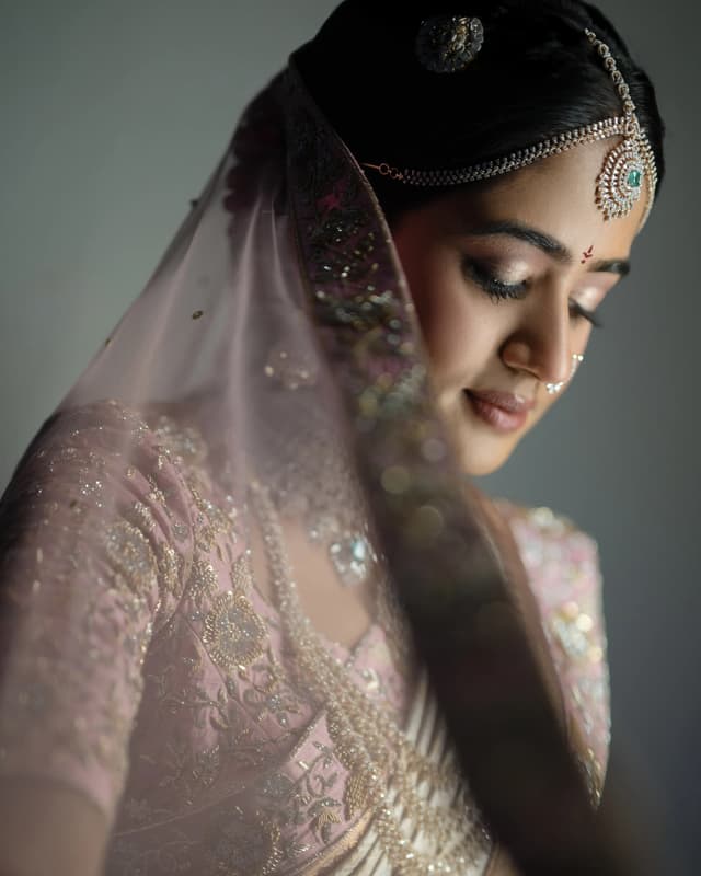 Bride in a pink wedding outfit looking down beneath her veil
